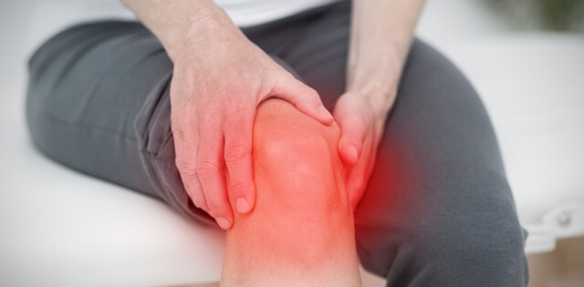 남자가 앉아서 오른쪽 바지를 허벅지까지 올리고 두손으로 무릎을 감싼다. 무릎에는 관절염에 관한 붉은 효과가 보인다.