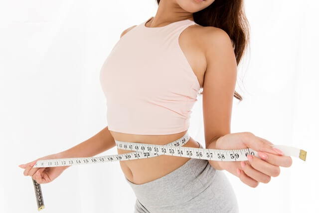 여자가 줄자로 허리사이즈를 재고 있는데 다이어트에 성공했는데 줄자가 넉넉히게 남아있다.
