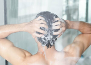남성이 샤워하면서 머리를 깜고 있다.